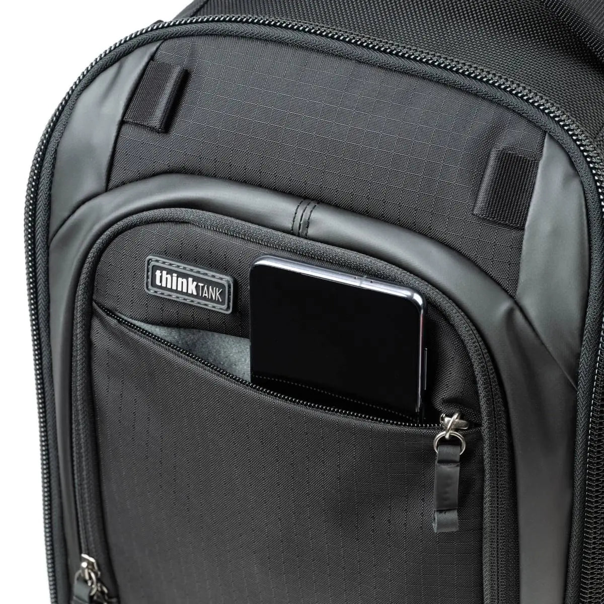 Black backpack with a pocket containing a smartphone and Think Tank logo.