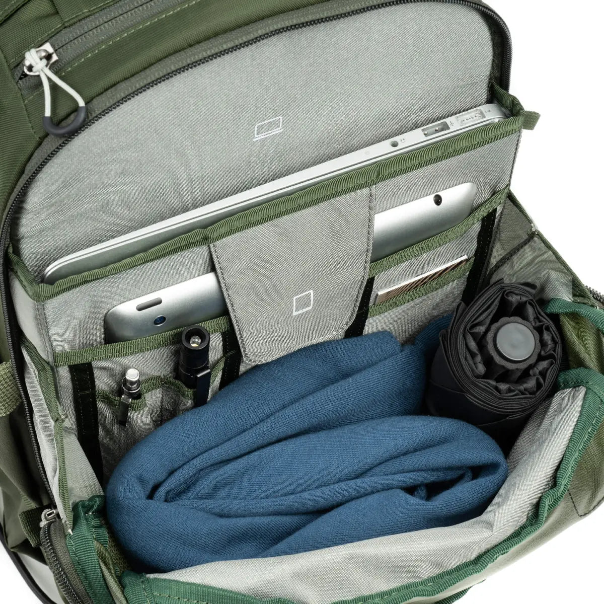 Open green backpack with compartments containing a blue blanket, electronic devices, and other items.