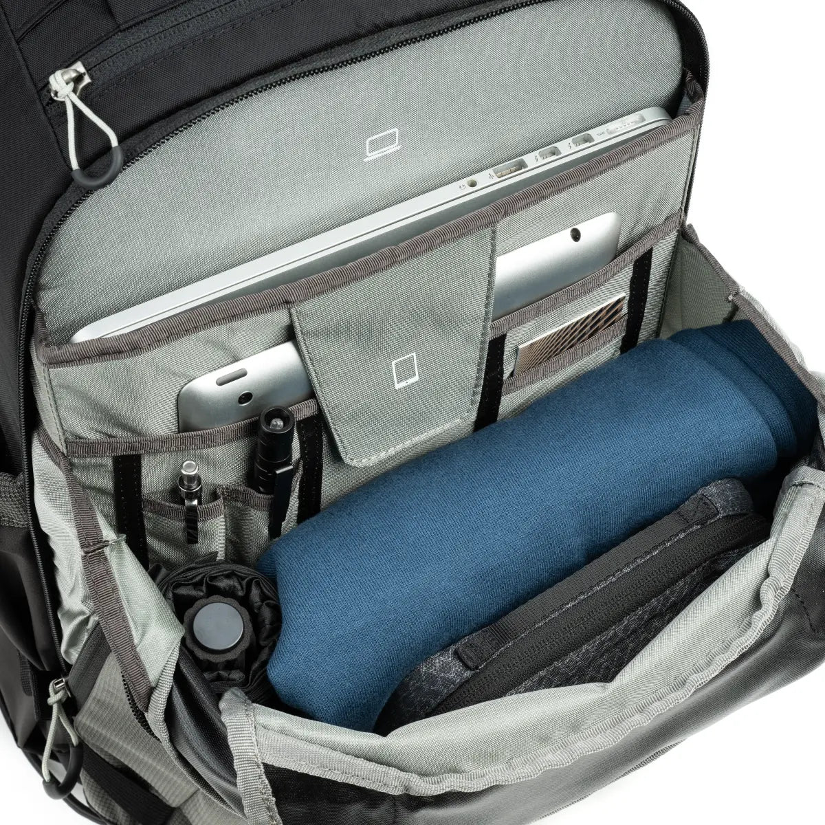 Open backpack with compartments containing a blue towel, water bottle, and electronic devices.