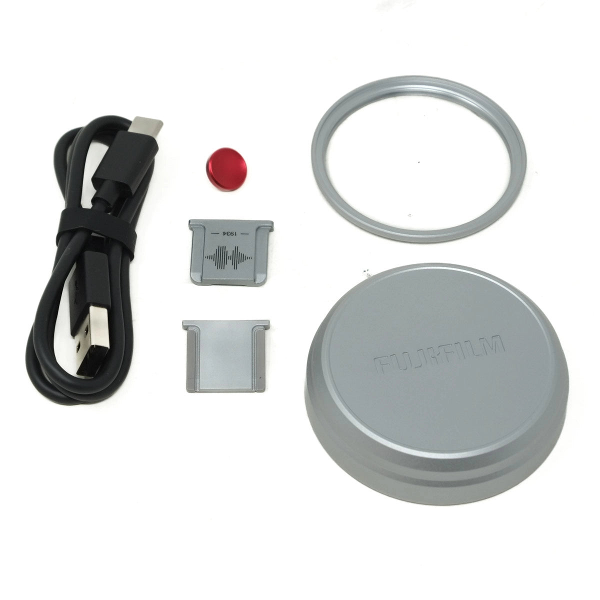 Set of electronic components including a cable, button, ring, and lid with Fujifilm branding on a white background.