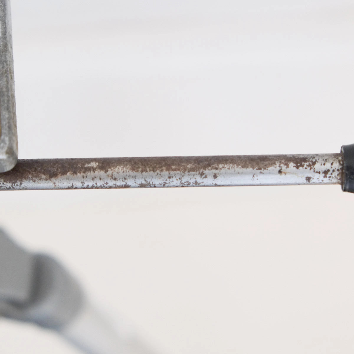 Close-up of a rusty metal tripod handle on a white background