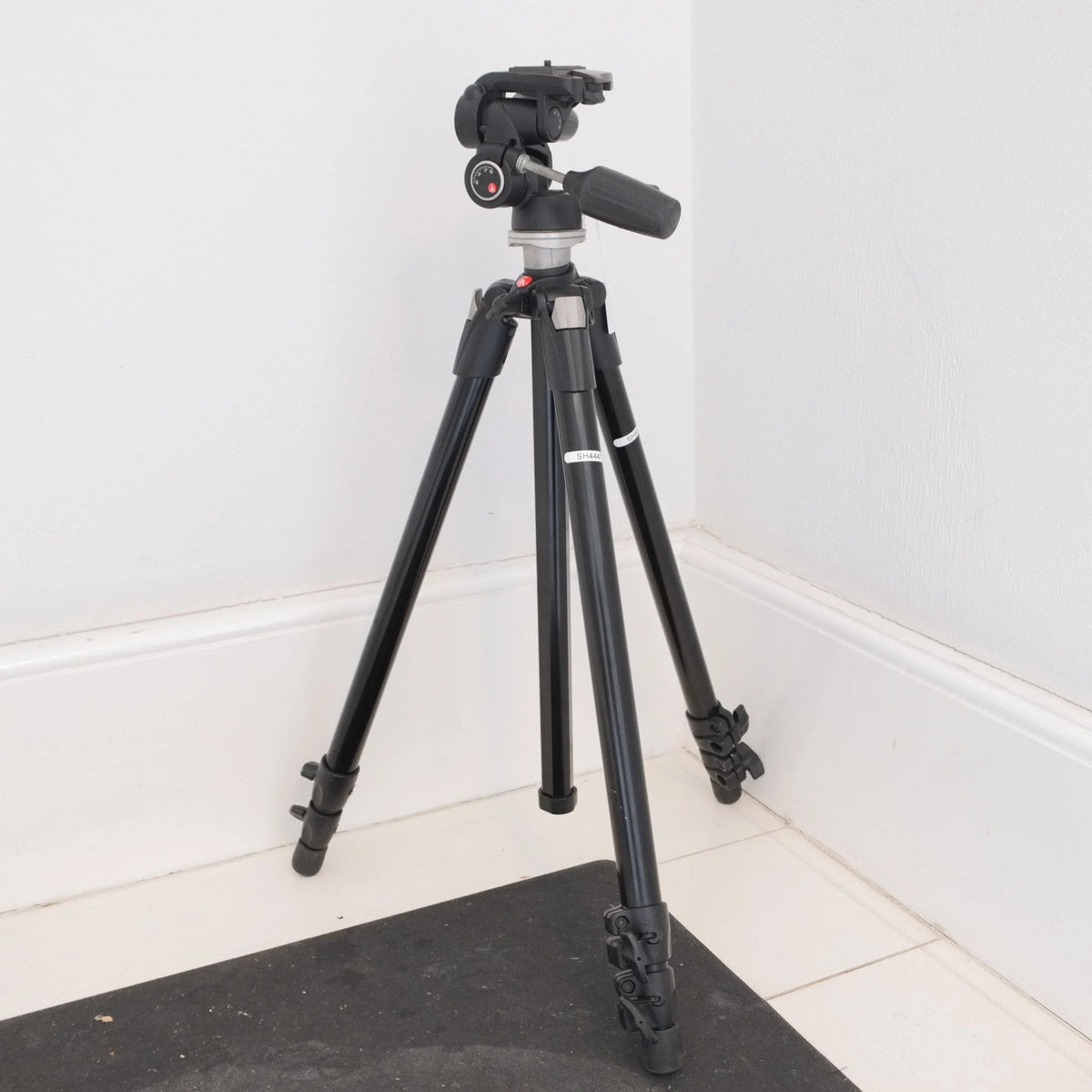 Black camera tripod on a white floor with a white wall background