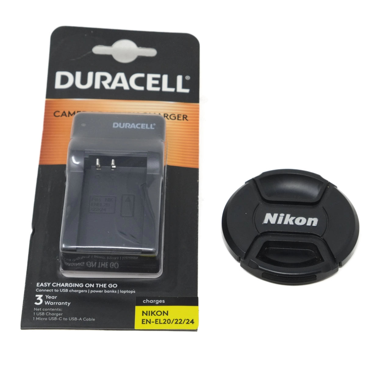Duracell camera charger and Nikon lens cap on a white background