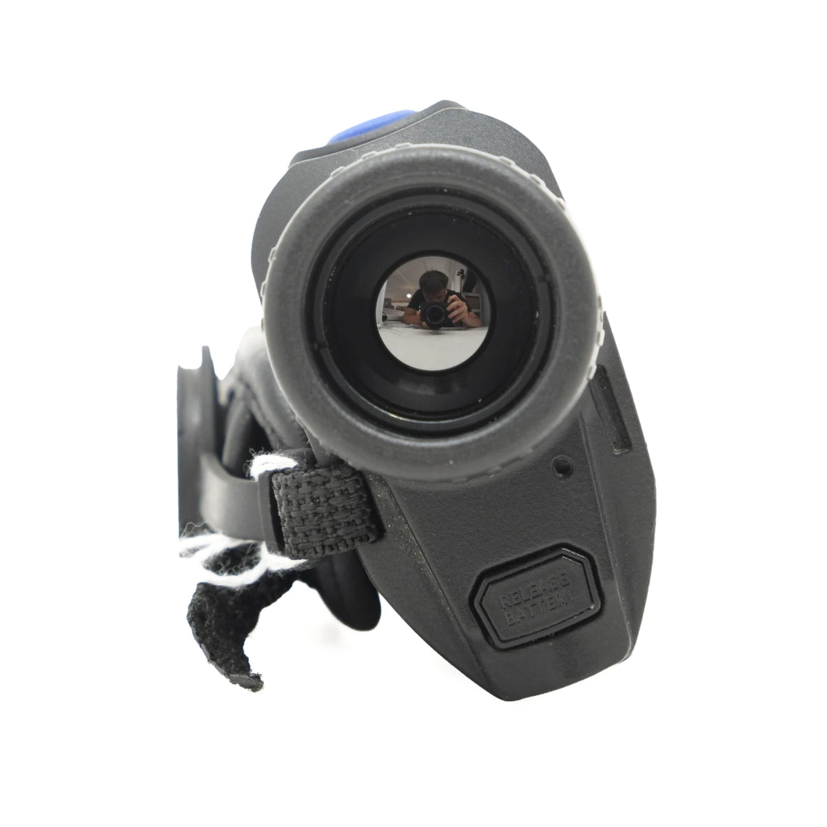 A black thermal imaging scope or camera lens device with a strap attachment, shown against a plain white background. The lens is facing forward, reflecting a photographer holding a camera.