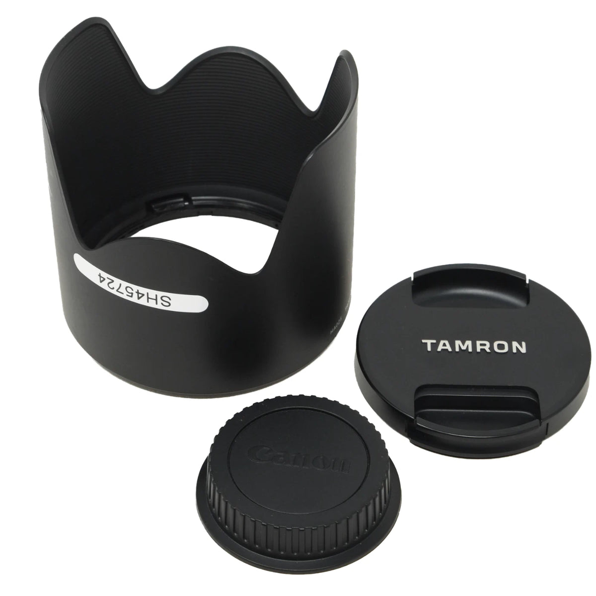 Black Canon Tamron lens hood and lens cap set, featuring a petal-shaped lens hood with a model number sticker and a separate lens cap with the Tamron logo.
