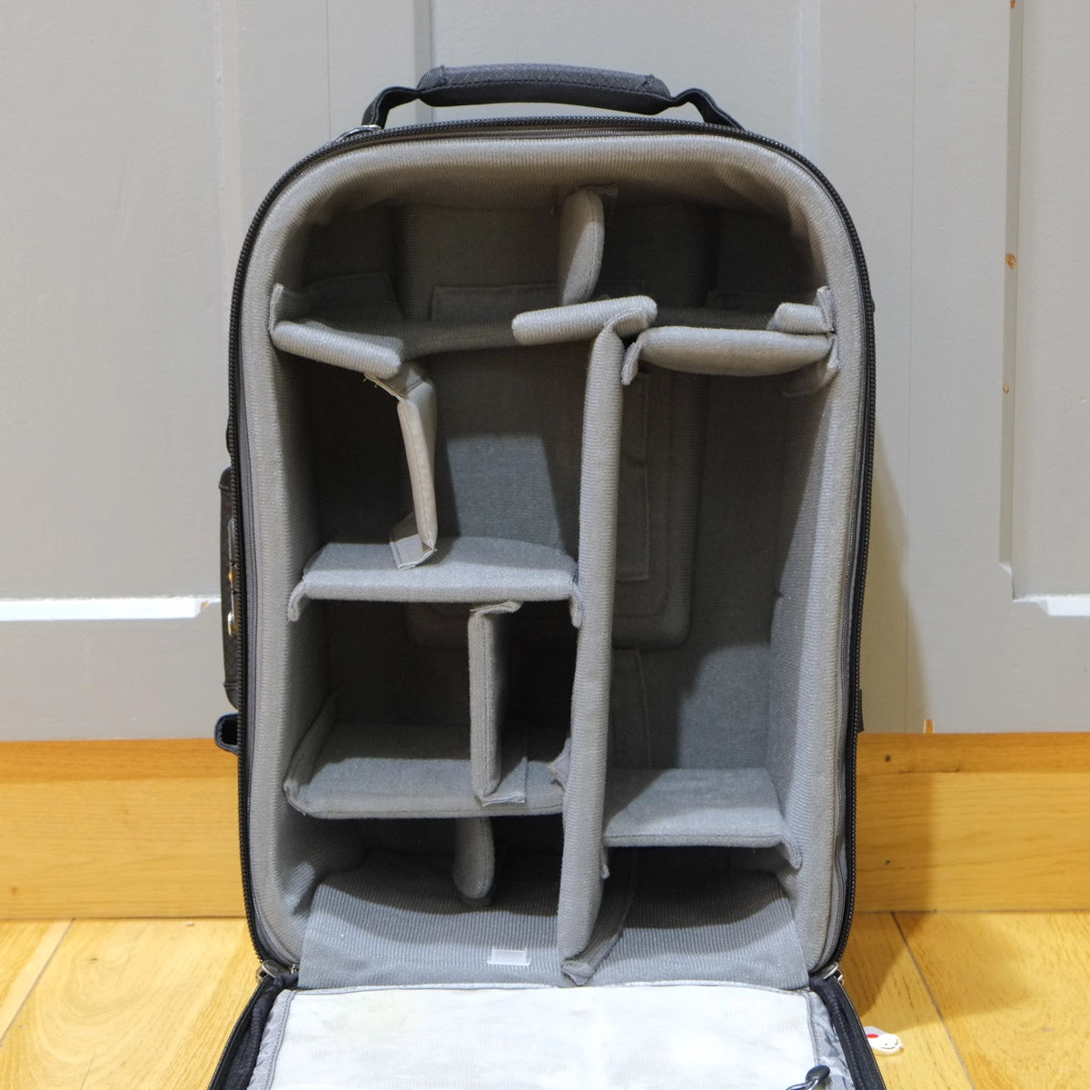 Gray camera bag with interior compartments on a wooden floor.