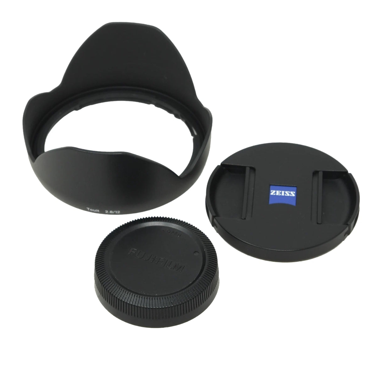Black camera lens accessories including a petal-shaped lens hood, a threaded lens cap embossed with FUJIFILM, and another lens cap with a blue ZEISS logo, shown on a white background.